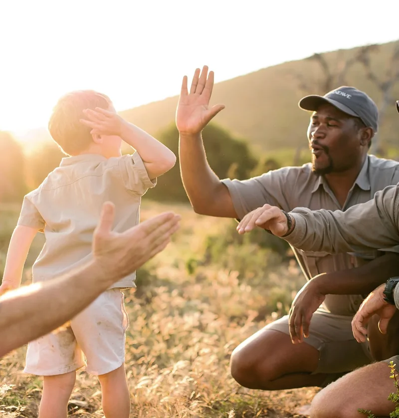 A child sharing a high-five with safari guides at Kwandwe Private Game Reserve