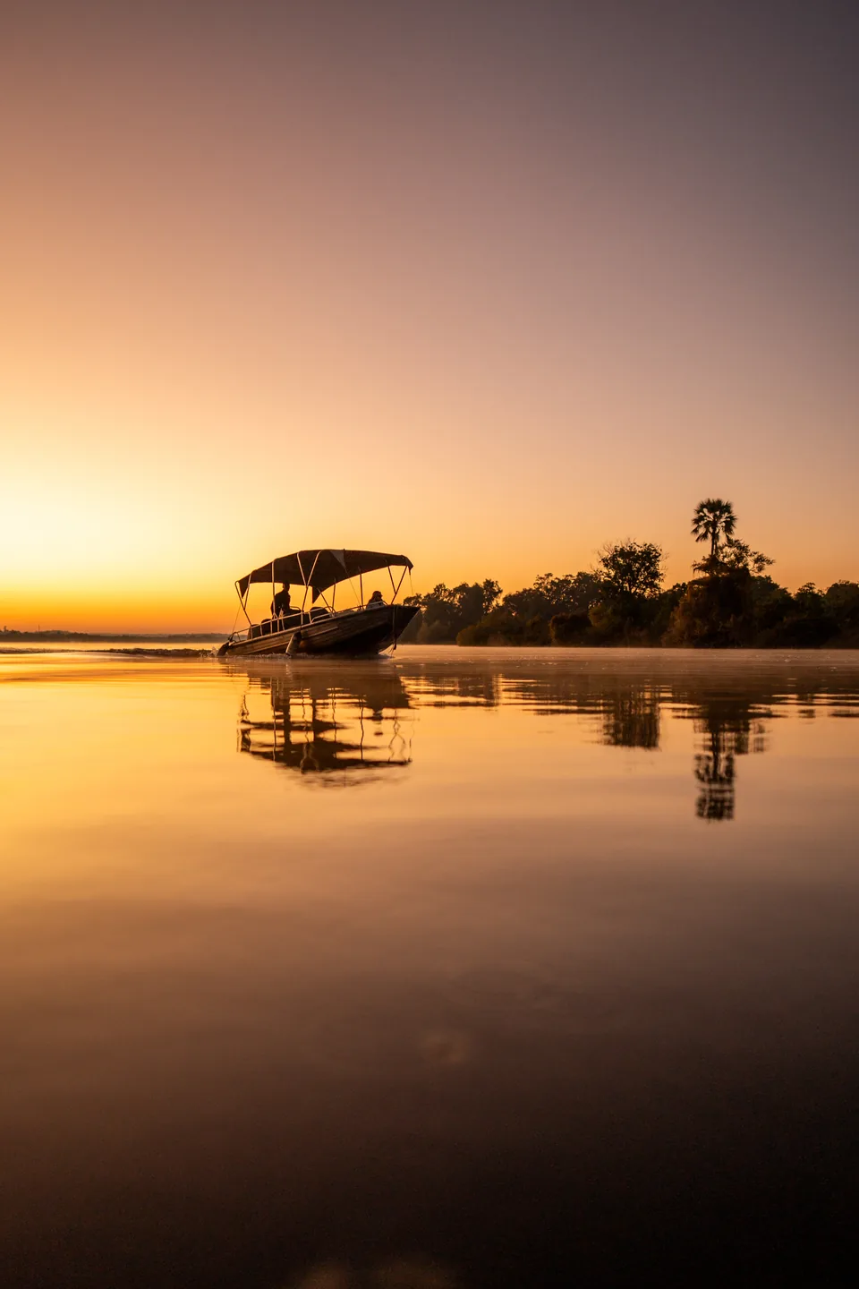 A river safari boat reflected in calm water at sunset