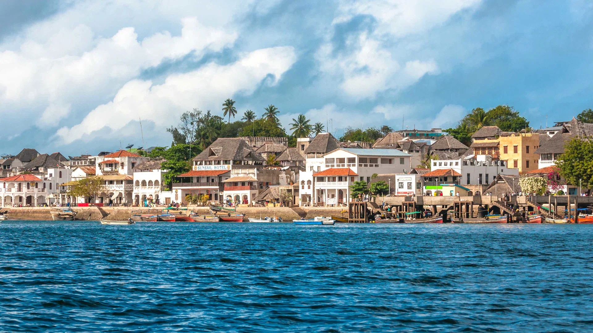 Lamu Island waterfront with traditional buildings, palms and boats beside the Indian Ocean.