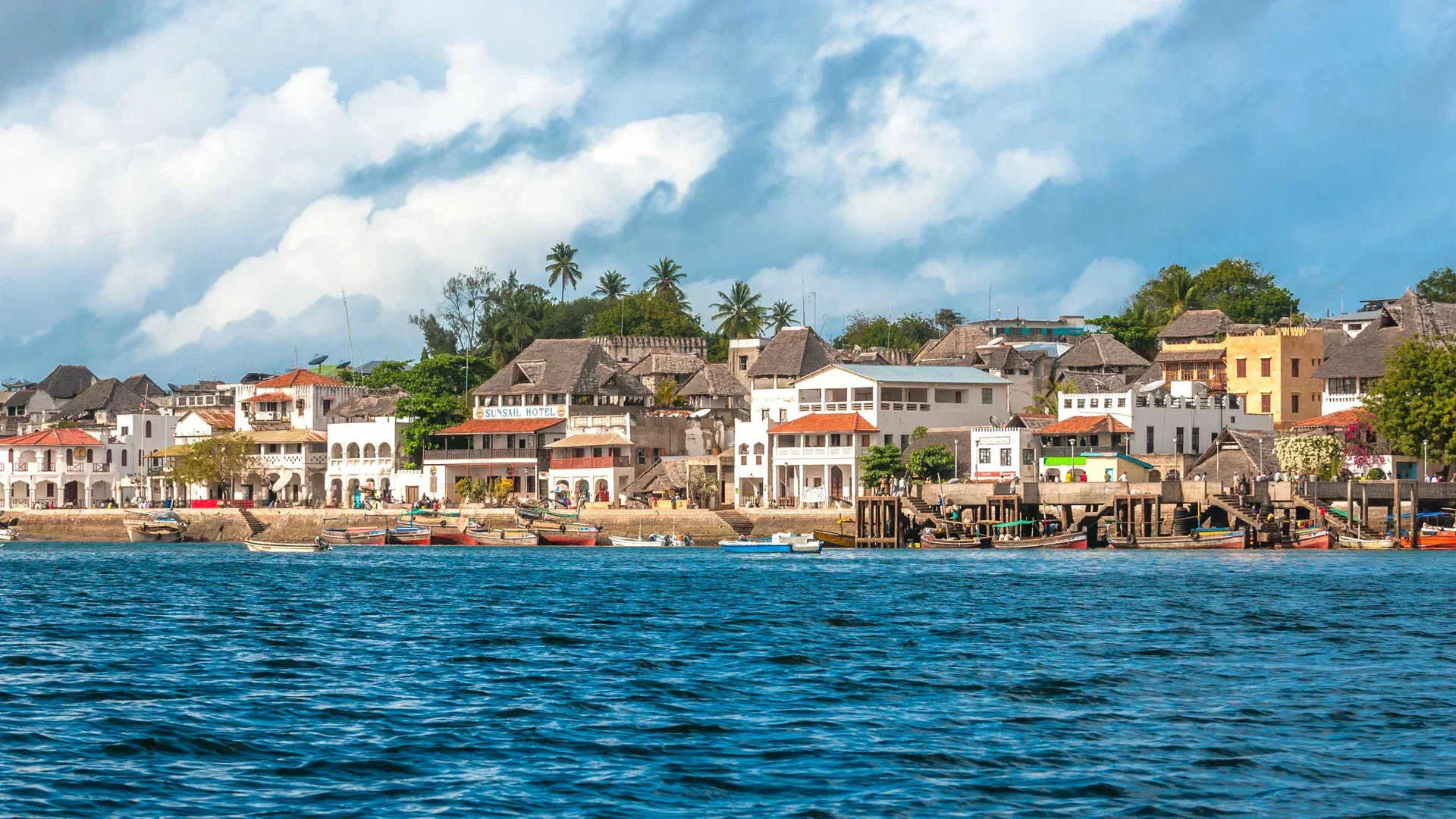 Lamu Island waterfront with traditional buildings, palms and boats beside the Indian Ocean.